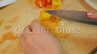 一个女人正在用一把刀在木板上切一个黄色和红色的樱桃番茄。